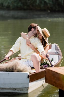 Romantik tekne gezisi sırasında hasır şapkalı genç bir kadın öpüşüyor. 