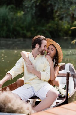 Hasır şapkalı mutlu genç kadın romantik tekne gezisinde gülümseyen adama sarılıyor. 