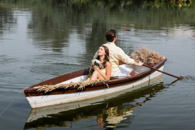Romantik tekne gezisi sırasında elinde çiçek tutan ve erkek arkadaşının sırtına yaslanan genç bir kadın. 