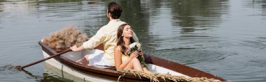 Romantik tekne gezisi sırasında elinde çiçek tutan ve erkek arkadaşının sırtına yaslanan genç bir kadın.