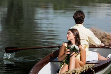 Romantik tekne gezisi sırasında elinde çiçeklerle erkeklerin sırtına yaslanan genç bir kadın. 