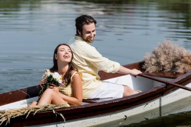 Romantik tekne gezisi sırasında elinde çiçekler ve erkek arkadaşının sırtına yaslanan mutlu genç bir kadın. 