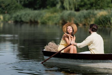 Hasır şapkalı gülümseyen kadın, adamla romantik tekne gezisi yapıyor. 