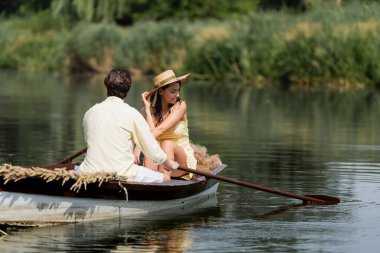 Hasır şapkalı neşeli kadın adamla romantik tekne gezisi yapıyor. 