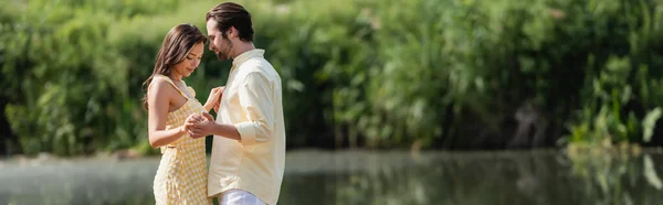 快乐的年轻夫妇穿着夏装 手牵手靠近湖畔 高举横幅 — 图库照片