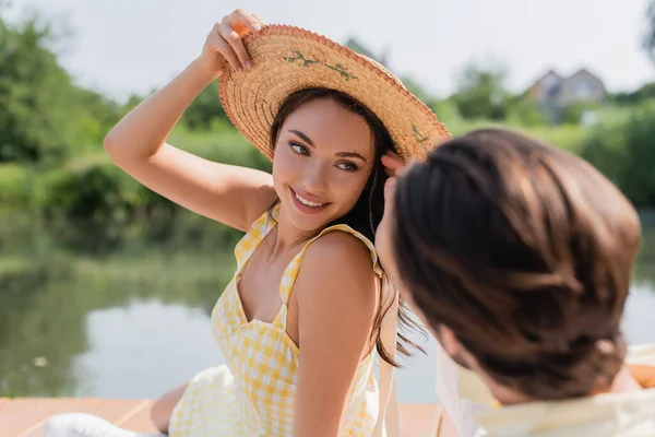 Uomo Sfocato Guardando Donna Sorridente Regolazione Cappello Paglia Mentre Vicino — Foto Stock