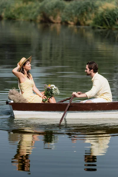笑容可亲的女人头戴草帽 捧着花 和男人一起乘浪漫的船 — 图库照片