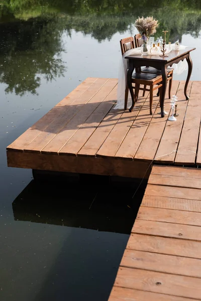 在湖边的木制码头上摆上浪漫的餐桌 — 图库照片