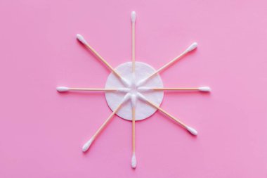 flat lay of cosmetic ear sticks near white cotton pad on pink background, top view