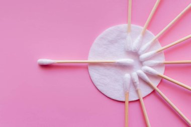 Pembe arka planda kozmetik pamuk pedin ve kulak çubuklarının üst görünümü