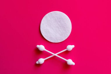 crossed ear sticks under white cotton pad on pink background, top view