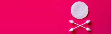 top view of crossed ear sticks near white cotton pad on pink background, banner