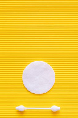 top view of white cotton pad and ear stick on yellow textured background