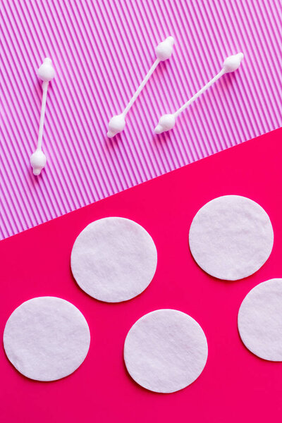 top view of white cotton pads and ear sticks on bicolor pink and violet background