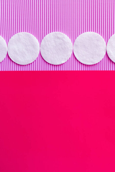 horizontal row of cotton pads on bicolor violet and pink background, top view