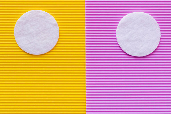 top view of two cotton pads on purple and yellow textured background