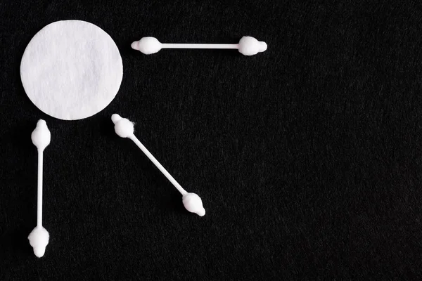Siyah arkaplanda beyaz pamuk pedin yanındaki kulak çubuklarının üst görüntüsü