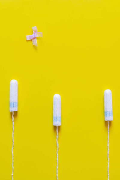 top view of bow near hygienic tampons on bright yellow background