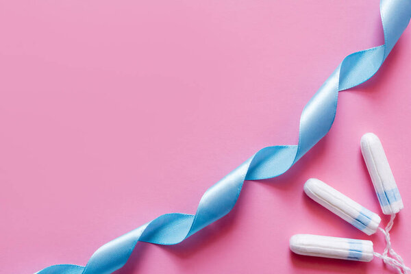 top view of blue satin ribbon near tampons on pink background