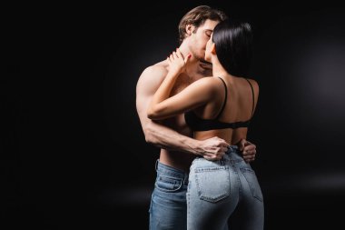 Passionate brunette woman kissing shirtless man on black background