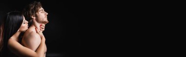 Side view of brunette woman touching neck of sensual boyfriend isolated on black, banner 