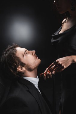Side view of man in suit looking at sensual girlfriend in silk dress on black background