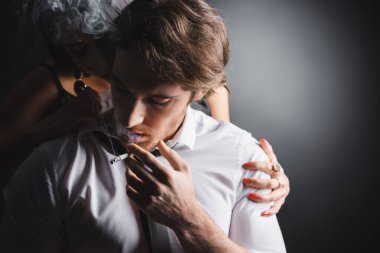 Young man in shirt smoking cigarette near girlfriend on black background