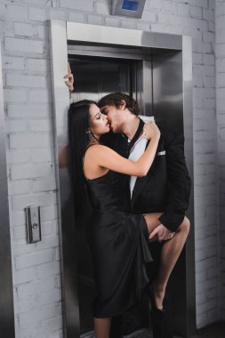 Passionate woman in dress undressing boyfriend near elevator 
