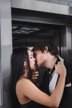 Sexy couple in formal wear kissing near elevator 
