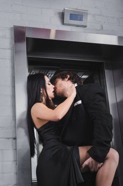 Passionate young couple in formal wear kissing near elevator 