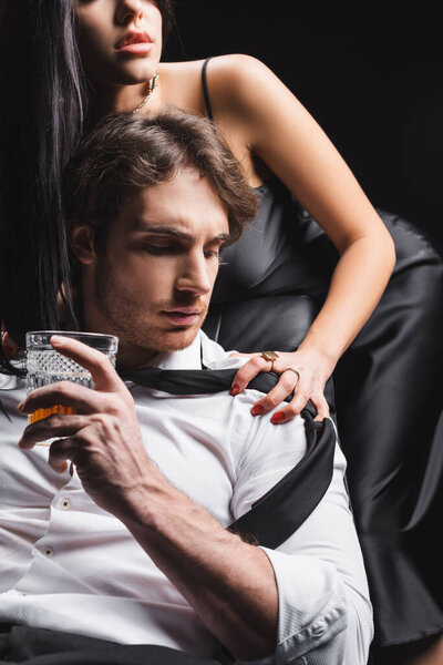 Sexy woman touching boyfriend in shirt holding whiskey isolated on black 