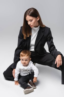 toddler boy sitting near young mom in black suit on grey