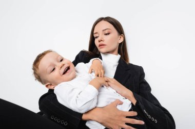 happy boy laughing near mother in black suit isolated on white