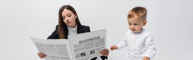 woman reading business newspaper near little son isolated on grey, banner