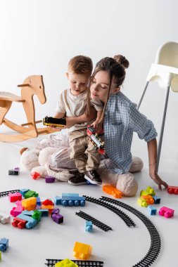 little boy with young mother playing with toy railway on white clipart