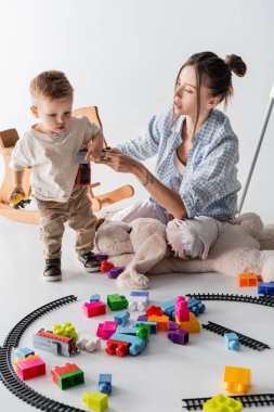 young woman holding toy train while playing with toddler son on white clipart