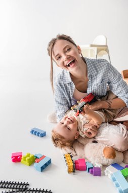 laughing woman looking at camera while playing with son on white