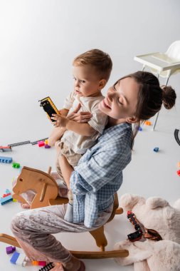high angle view of joyful woman riding rocking horse together with son on white