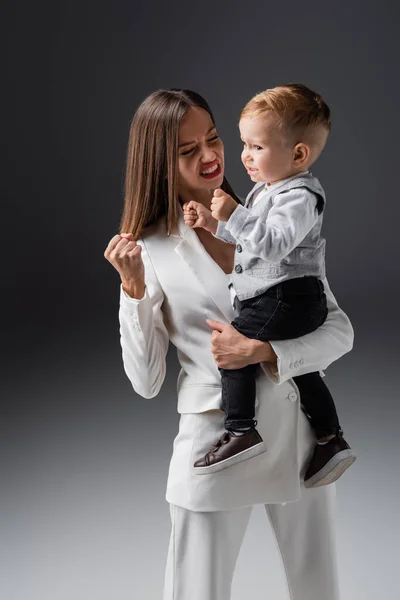 excited mother and son showing win gesture on grey