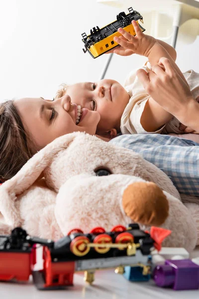 happy woman and boy with toy train lying near blurred soft toy isolated on white