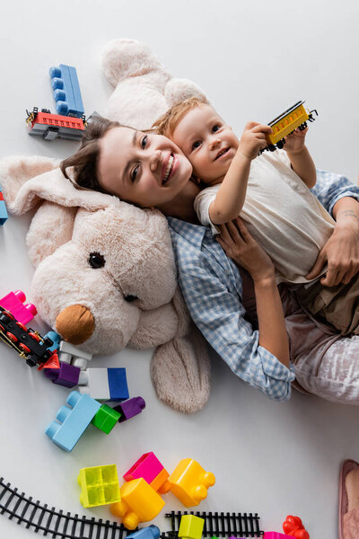 top view of happy woman lying with toddler son on toy dog on grey