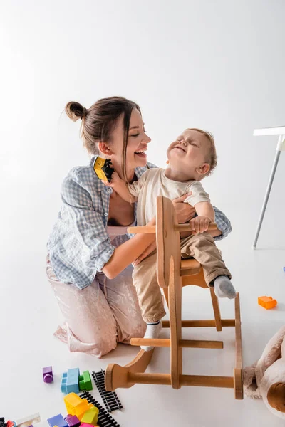 Happy Woman Hugging Cheerful Son Riding Rocking Horse White — Foto Stock