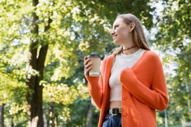Düşük açılı, mutlu bir kadının elinde kahve bardağıyla gidişi.