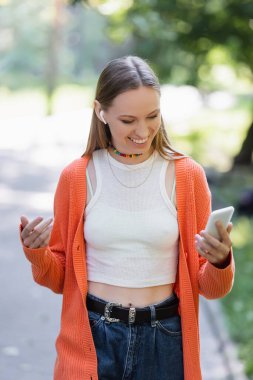 Green Park 'ta cep telefonu kullanan kablosuz kulaklıklı pozitif kadın.