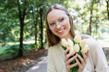 happy woman in glasses holding tulips in green park