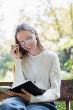 Yeşil Park 'ta elinde defter tutarken gözlüklerini ayarlayan neşeli kadın.
