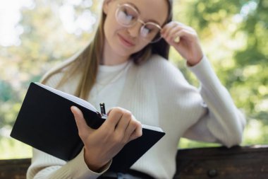Bulanık gözlüklü kadın elinde defter ve kalem tutuyordu.