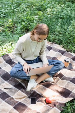Yüksek açılı, gözlüklü, bacak bacak üstüne atmış ve dizüstü bilgisayar kullanan serbest çalışan biri. 