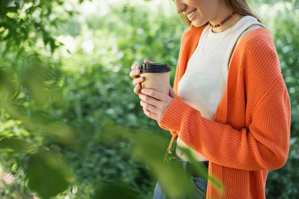 微笑的女人拿着装有咖啡的纸杯在绿园里散步的剪影 — 图库照片