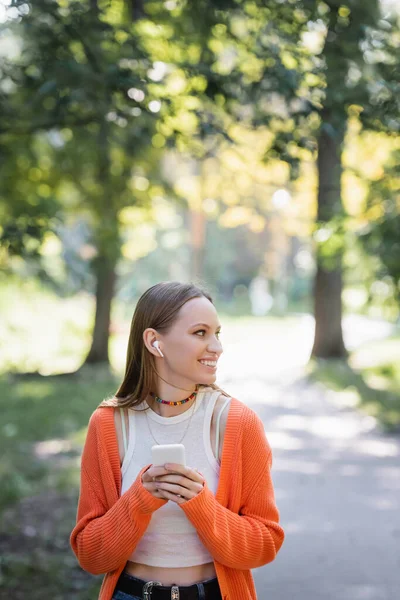 Pleased Woman Orange Cardigan Wireless Earphone Using Smartphone Park — Stok fotoğraf